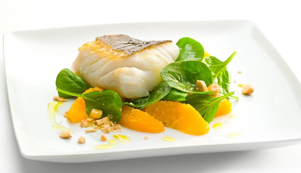 Skrei Noruego, sobre lienzo de espinacas y naranja