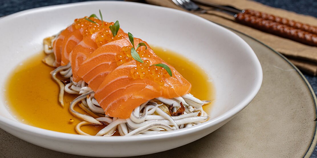 Salmón noruego fresco en láminas sobre gulas salteadas en ajo y guindilla, en caldo corto de setas